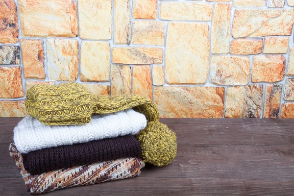 Stack of knitting clothes on wooden table opposite a stony wall — Stock Photo, Image