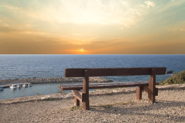 Houten bench op het strand tegen de ondergaande zon — Stockfoto