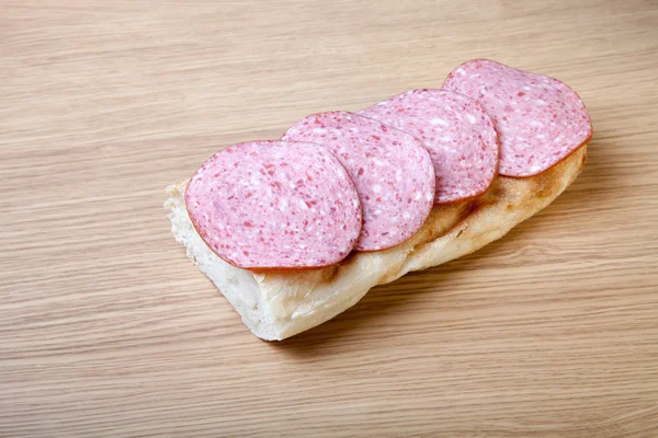 Sandwich of white bread with slices of sausage on a light wooden — Stock Photo, Image
