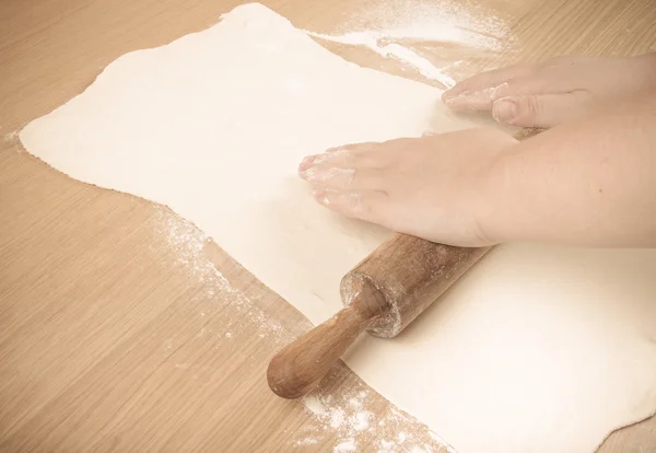 Толстые женские руки выкатывают тесто на легкий деревянный стол . — стоковое фото