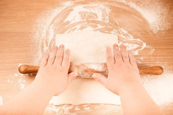 Plump women's hands roll out the dough on a light wooden table. — Stock Photo, Image