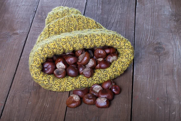Châtaignes dans un chapeau tricoté sur une vieille table en bois — Photo