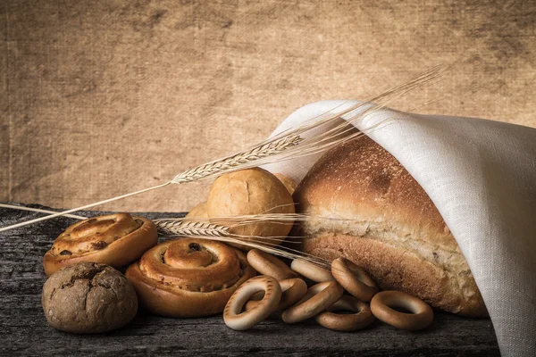 Different types of fresh bread and wheat ears on old wooden tabl — Stock Photo, Image