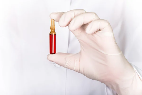 A gloved hand holding a ampoule with medicine on a background of — Stock Photo, Image