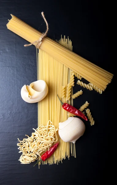 Different kinds of pasta and  red chili pepper on a black backgr — Stock Photo, Image