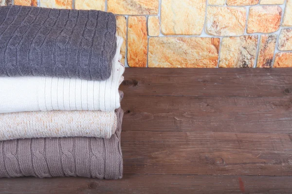 Stack of knitting clothes on wooden table opposite a stony wall — Stock Photo, Image