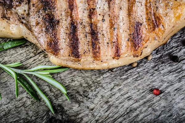 Pork steak with rosemary and pepper on old wooden table. Toned — Stock Photo, Image