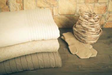 Stack of knitting clothes, hat and mittens on wooden table oppos