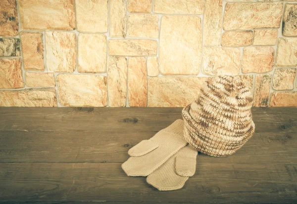 Chapeau et mitaines tricotés sur une table en bois face à un mur pierreux. Pour — Photo