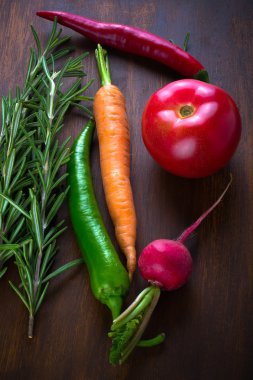 Vegetables and herbs with sea salt on brown cutting board. Toned