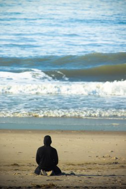 Okyanus dalgaları seyretmekten kum plajındaki bir yalnız adam. Tonda