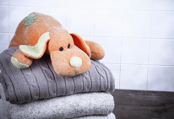 Knitted toy dog on the stack of knitted clothes on wooden table