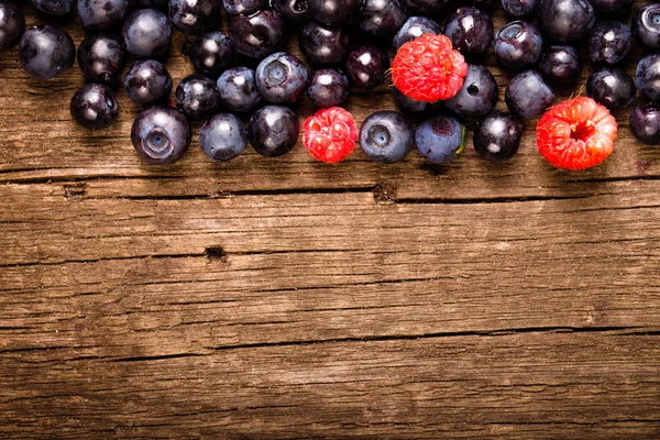 Forest blueberries and raspberries on an old wooden board — Stock Photo, Image