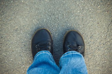 Mavi kot pantolon ve siyah çizmeler bacaklarda üstten görünüm asphal üzerinde
