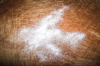 White wheat flour is scattered on an old worn cutting board. Bac