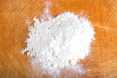 Pile of white wheat flour is scattered on an old worn cutting bo