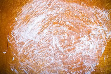 White wheat flour is scattered on an old worn cutting board. Bac
