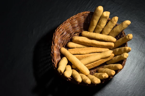 Bastoncini di formaggio appena sfornati in un cesto di legno di vimini sulla linguetta nera — Foto Stock