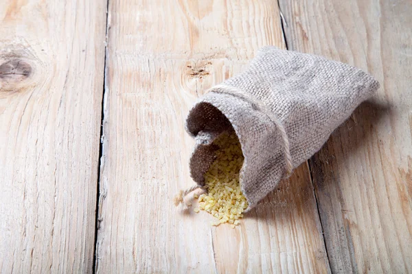 Groat pours out of the bag on a wooden table made of old boards — Stock Photo, Image