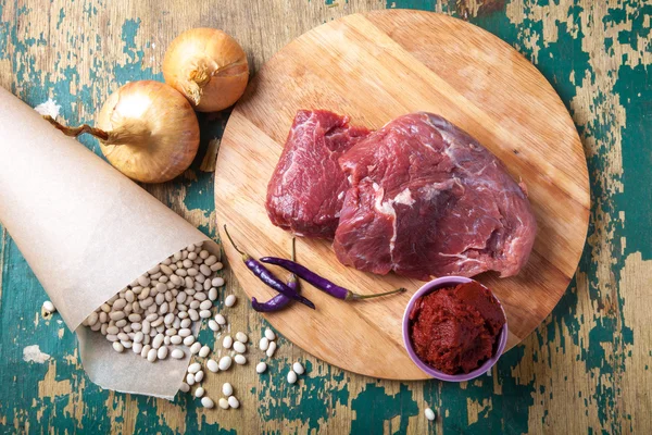 Fresh raw meat, white bean and vegetables on an old wooden table — Stock Photo, Image