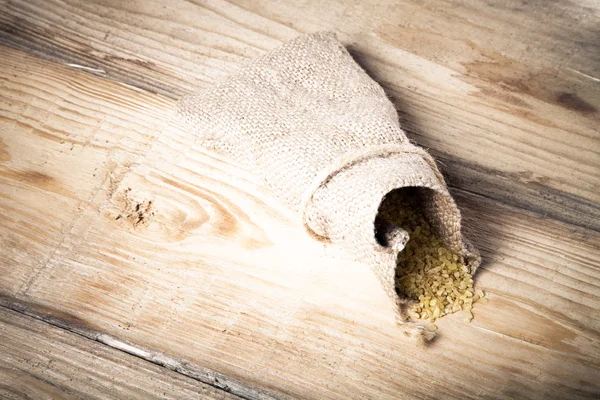 Groat pours out of the bag on a wooden table made of old boards. — Stock Photo, Image