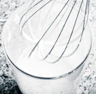 Whisk and whipped cream in a tall glass on the kitchen table. To