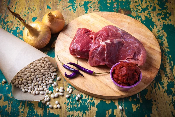 Fresh raw meat, white bean and vegetables on an old wooden table — Stock Photo, Image