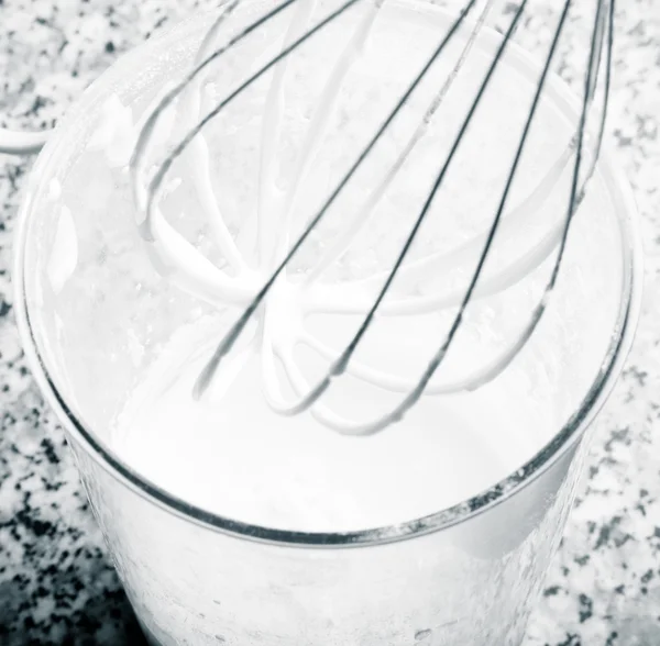 Whisk and whipped cream in a tall glass on the kitchen table. To — Stock fotografie