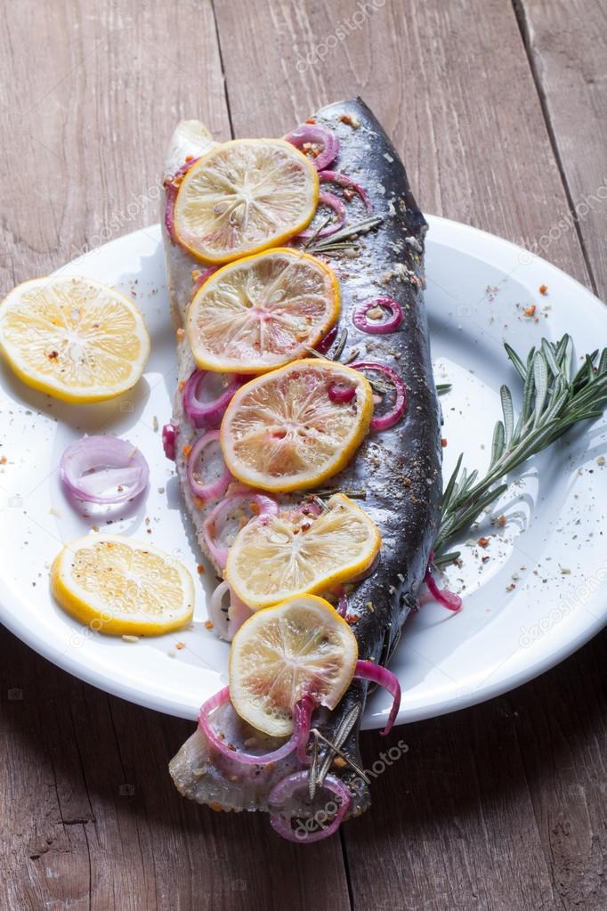 Fish Nelma with lemon, onion and rosemary on a wooden table