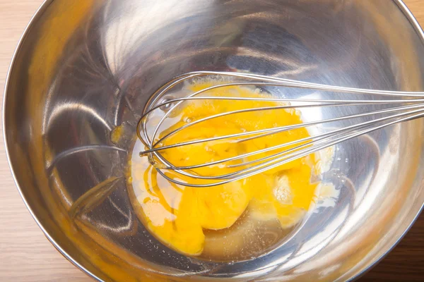 Broken eggs in a metal bowl with whisk — Stock Photo, Image