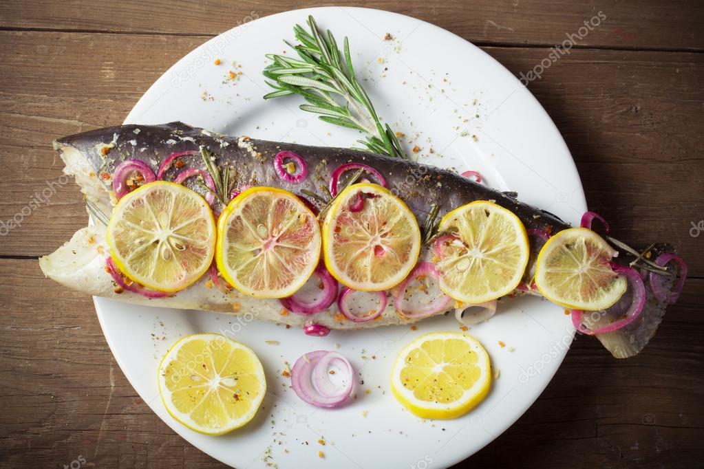 Fish Nelma with lemon, onion and rosemary on a wooden table. Ton