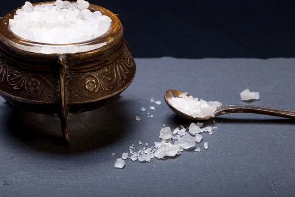 Sea salt in an old salt shaker on a plate of slate on a black ba — Stock Photo, Image