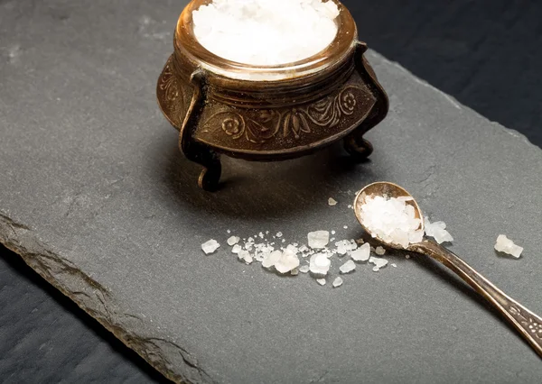 Sea salt in an old salt shaker on a plate of slate on a black ba — Stock Photo, Image