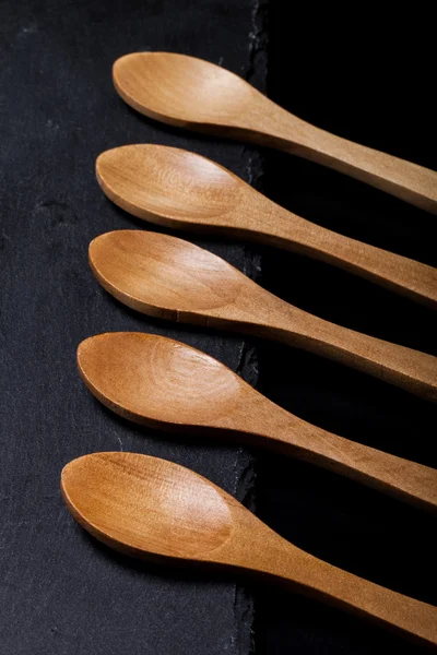 Wooden spoons on a plate of slate on a black background — Stock Photo, Image