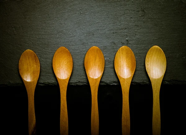 Wooden spoons on a plate of slate on a black background. Toned — Stock Photo, Image
