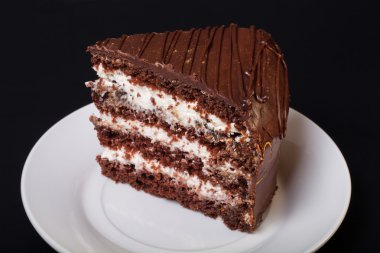 Siyah arka plan üzerine beyaz tabakta çikolatalı pasta bir parça