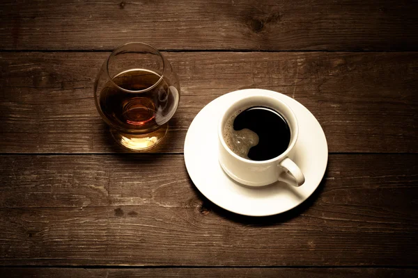 Xícara branca de café e conhaque em um copo na velha mesa de madeira. T — Fotografia de Stock