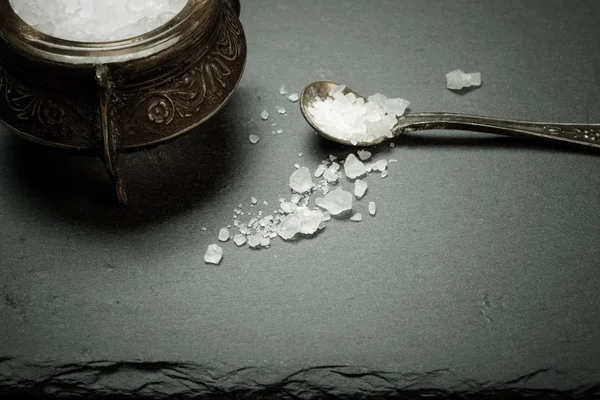 Sea salt in an old salt shaker on a plate of slate on a black ba — Stock Photo, Image