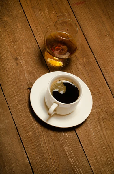 Xícara branca de café e conhaque em um copo na velha mesa de madeira. T — Fotografia de Stock