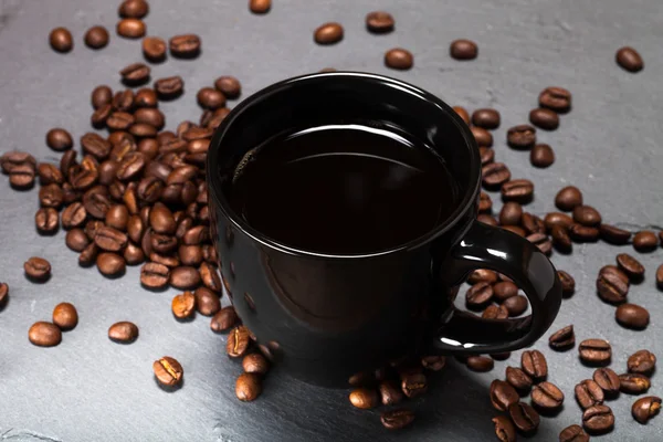 Xícara preta de sementes de café e café no fundo da ardósia — Fotografia de Stock