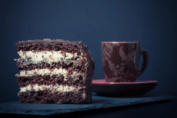 Um pedaço de bolo de chocolate e xícara de café na placa de ardósia em bl — Fotografia de Stock