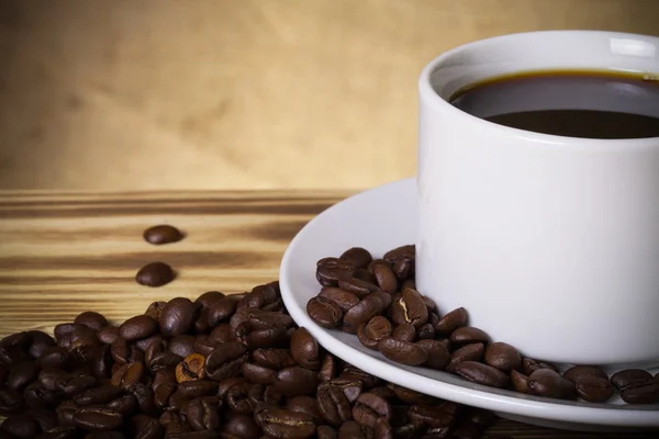 Kaffeebohnen und Kaffee in weißer Tasse auf Holztisch gegenüber — Stockfoto