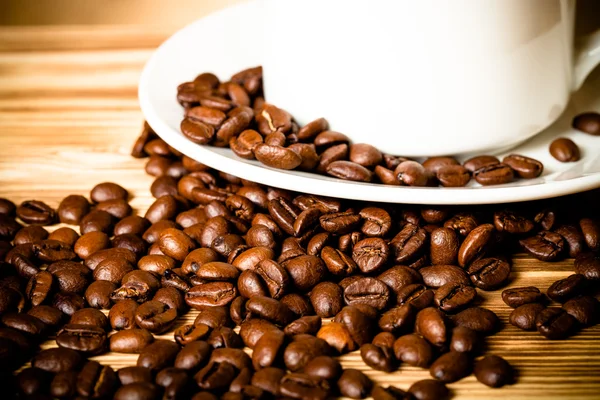 Kahvipavut ja kahvi valkoinen kuppi puinen pöytä backgro — kuvapankkivalokuva