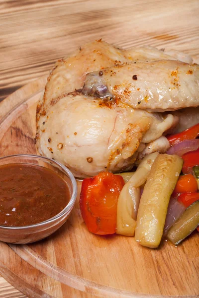 Chicken with vegetables served on round cutting board on burned — Stock Photo, Image