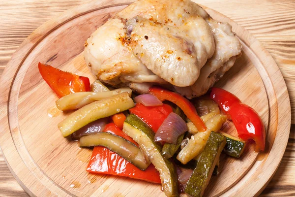 Pollo con verduras servido sobre tabla de cortar redonda sobre quemado —  Fotos de Stock