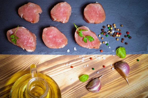 Pieces of raw meat on a plate of slate herbs spices and olive oi — Stock Photo, Image