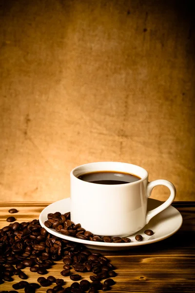 Kaffeebohnen und Kaffee in weißer Tasse auf Holztisch gegenüber — Stockfoto