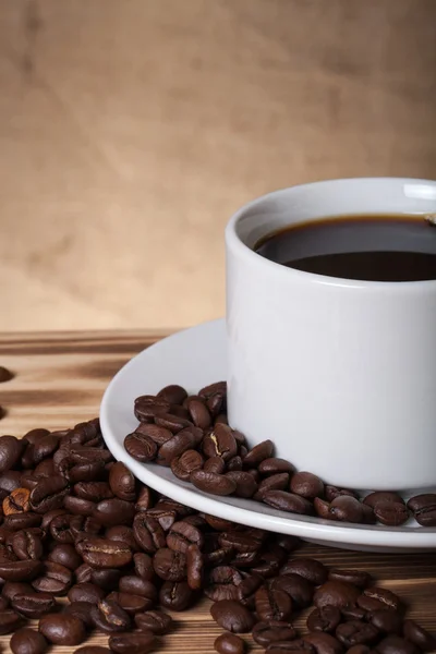 Granos de café y café en taza blanca en la mesa de madera frente a un — Foto de Stock