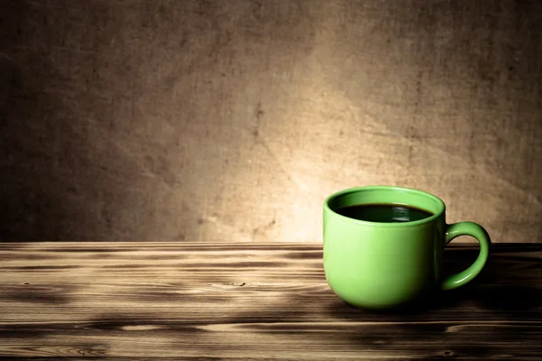 Káva v šálku na dřevěný stůl naproti pytlovina rozostřeného pozadí — Stock fotografie