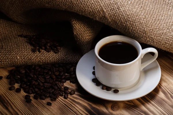 Café frijoles y café en taza blanca sobre mesa de madera con arpillera — Foto de Stock